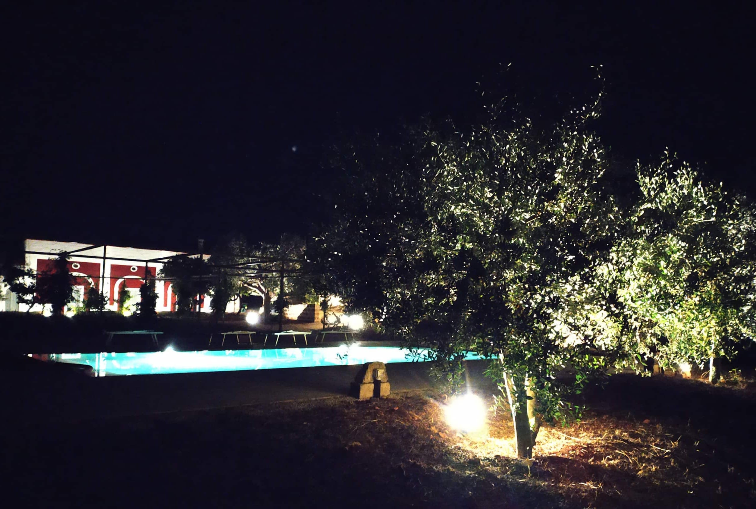 La piscine illuminée à la nuit tombée, eau turquoise lumineuse devant la façade éclairée