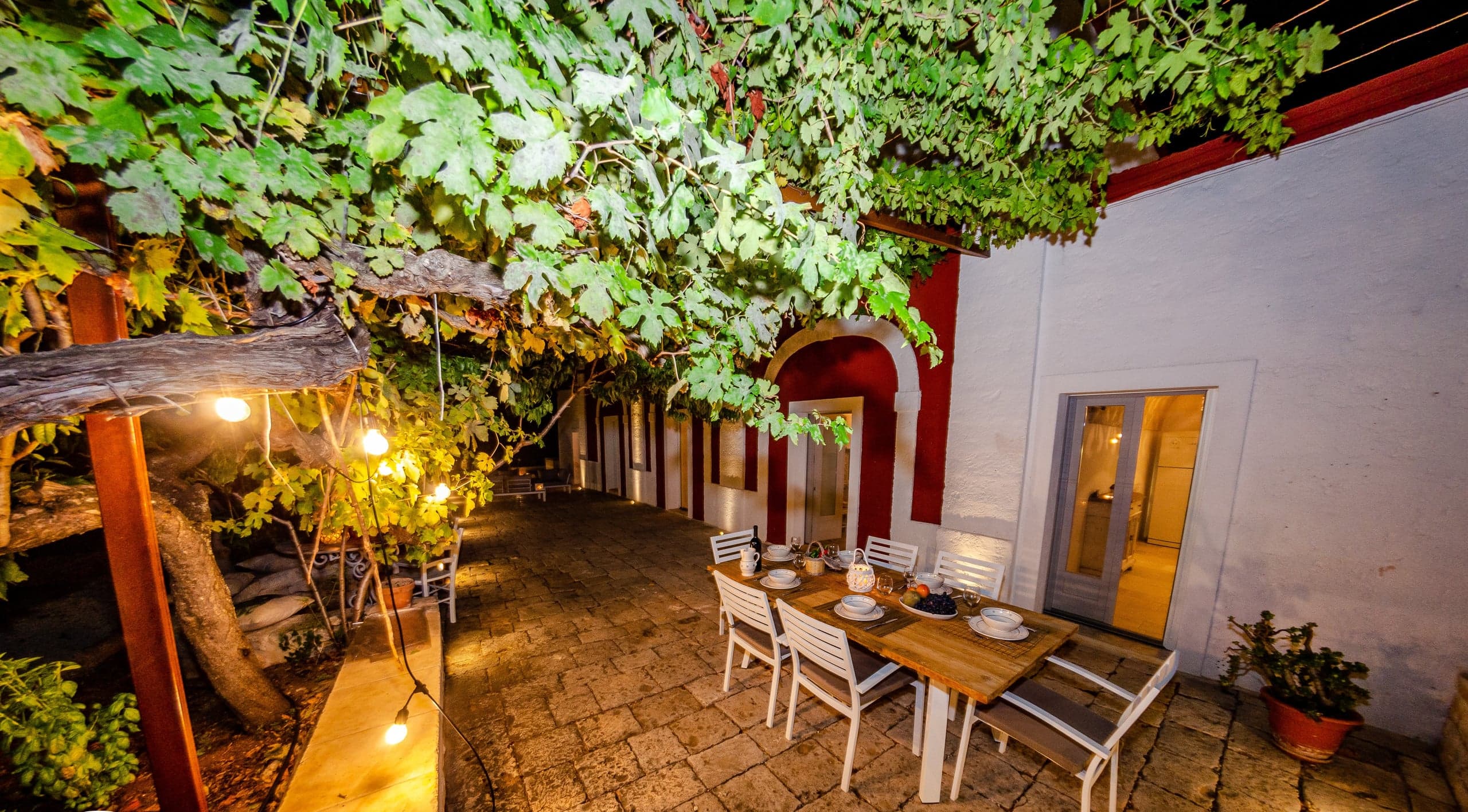 La table du dîner dressée sur la terrasse à la tombée du jour, sous les guirlandes