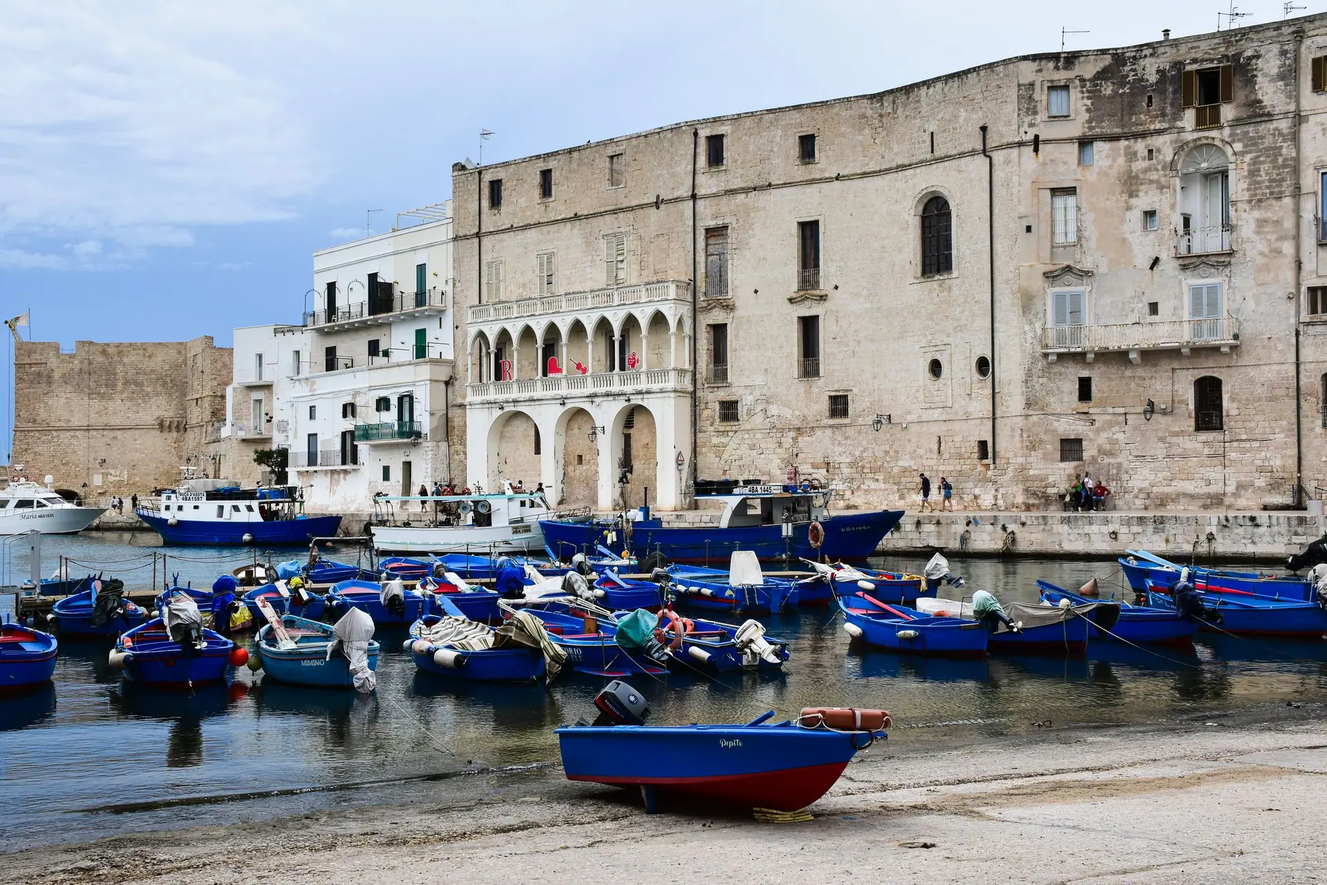 Des barques de pêche bleues amarrées serrées dans le port ancien de Monopoli, au pied des remparts