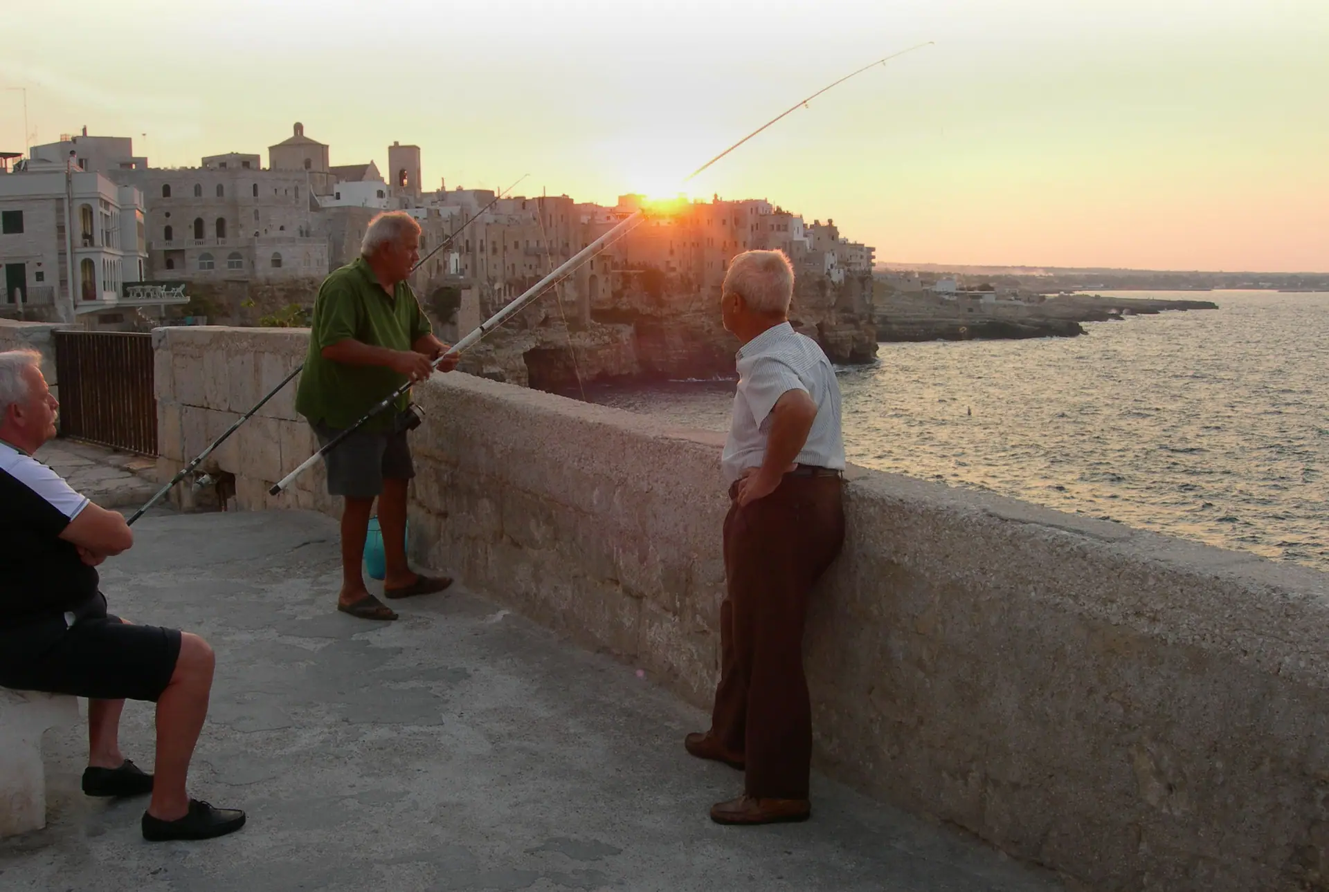 Des pêcheurs à la ligne sur les remparts de Polignano a Mare, au coucher du soleil