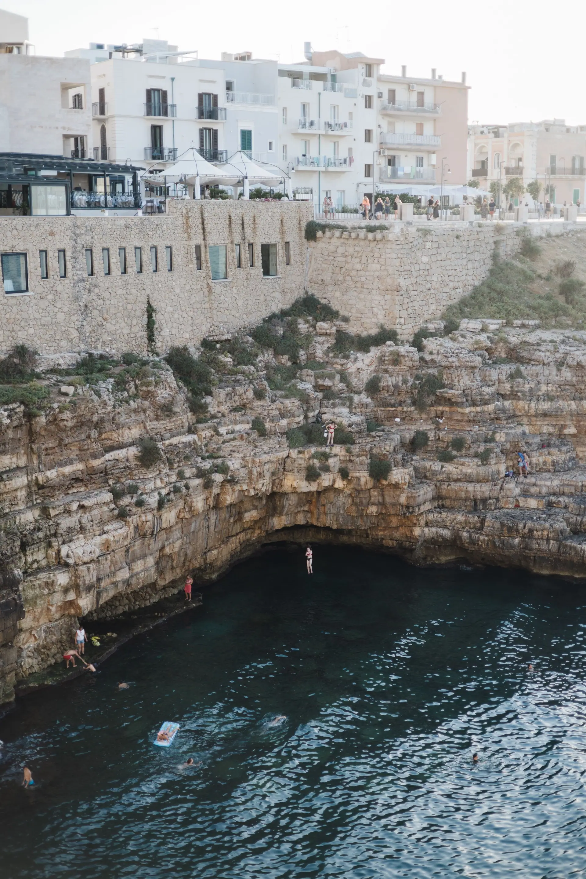 Un plongeur saute dans une crique encaissée sous une arche rocheuse, à Polignano a Mare